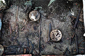 Blick in die Baugrube mit Pfählungen für das Gebäude und prähistorischen Holzresten. Zu erkennen sind rechtwinklig liegende Hölzer und ein massiver, angespitzter Pfahl (Pfeil). Foto: LAD, W. Hohl